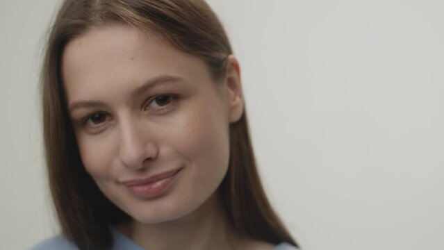 Smiling brunette woman looks at the camera and tucks her hair behind her ear. Portrait shooting in the studio on a white background.