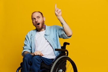 A man in a wheelchair surprised, with tattoos on his arms sits on a yellow studio background, the concept of health is a person with disabilities