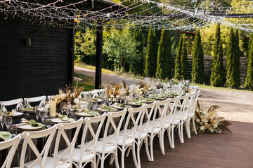 Wedding decorations. Served wedding table with white chairs golden plates, green napkins, decorative fresh and dried flowers, candles and and light bulbs. Celebration details, wedding outdoor
