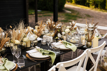 Wedding decorations. Served wedding table with golden plates, green napkins, decorative fresh and dried flowers, candles and and light bulbs. Celebration details, wedding outdoor