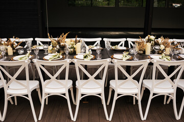 Wedding decorations. Served wedding table with white chairs golden plates, green napkins, decorative fresh and dried flowers, candles and and light bulbs. Celebration details, wedding outdoor
