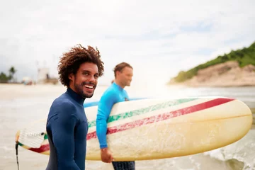 Tuinposter brazilian mid adult  surf tutor entering the water with his student to surf the waves in Brazil © oscargutzo