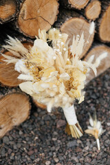 Bridal bouquet and boutonniere from different dried flowers of neutral colors on the background of logs. Wedding concept