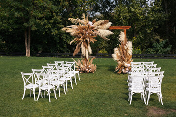 Square wedding arch decorated with reeds with white chairs. Wedding ceremony in the forest outdoor 