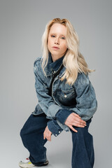 Fototapeta na wymiar young blonde model in trendy denim outfit looking at camera isolated on grey.