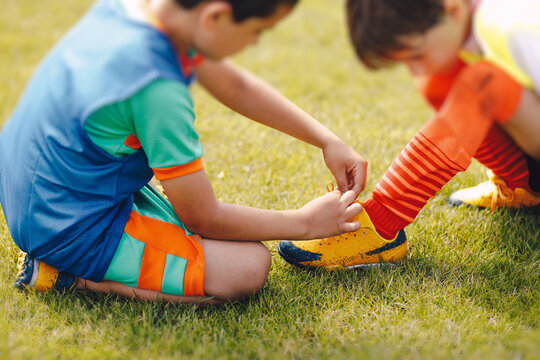 Young boy helping to friend in tiying shoelaces. Children tie shoelaces at grass sports field. Little boy helping to friend with tying shoelaces in soccer cleats