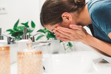 Close up side view woman leaning down in the sink washing her face with water 