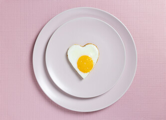 Fried eggs in the shape of a heart on pink plates and a pink background. Breakfast on Valentine's Day.