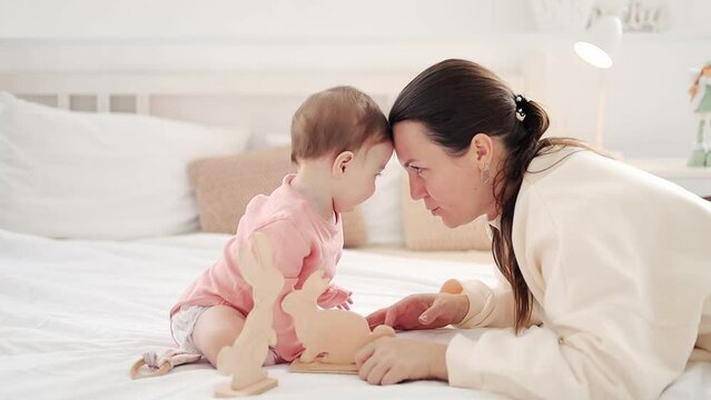 mom plays with her little daughter with wooden toys at home on the bed and have fun together, family and motherhood.
