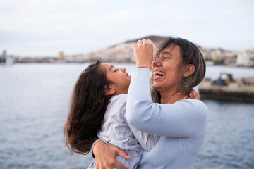 Glad and happy mother and daughter hugging and laughing outdoors near the sea. Concept: Lifestyle, motherhood, hug