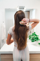 Back view, vertical photo unrecognizable woman brushing her long brown hair 