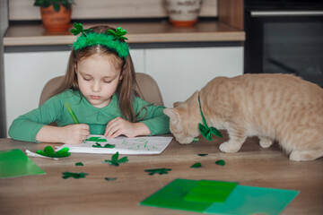 A little girl with a bandage on her head draws and cuts green shamrocks for St. Patrick's Day at a...