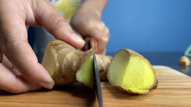 Female hands cutting organic raw ginger root slice on a wooden chopping board at kitchen close up shot slow motion. Natural herbal recipe concept