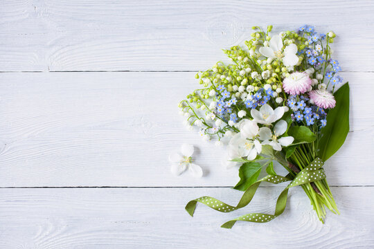 Bouquet of spring lilies of the valley, forget me not, flowers, daisies, apple blossoms and ribbon on white wooden background, copy space
