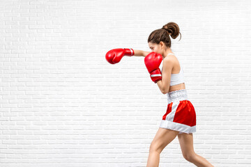 Young woman in red boxing gloves and boxer shorts works out the jab indoor on loft white background.