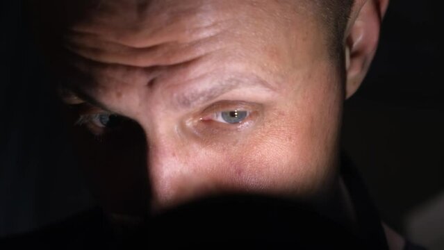 A man examines something in detail in the dark, close-up