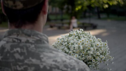 The guy in a military uniformcarries a bouquet of flowers. Romantic military man going with bouquet of field daisies. Shooting in motion. Back view.
