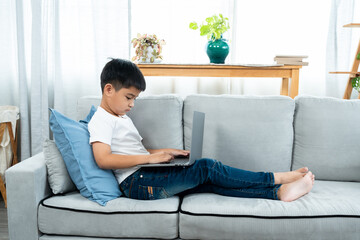 Asian boy sitting open notebook, studying online morning, sitting on living room sofa house, looks determined to study, When class was finished, they sat down to do homework that teacher ordered.