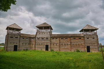 Fototapeta premium An old wooden fortress surrounded by a fence with sharp peaks on a foggy rainy day.