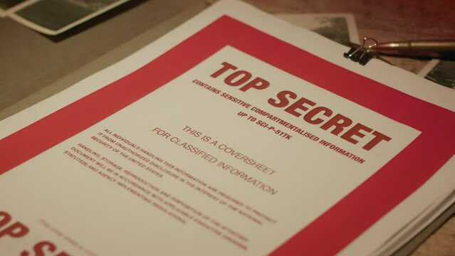 A retro manilla folder containing documents marked 'Top Secret' is seen on a wooden table lit by subdued light.