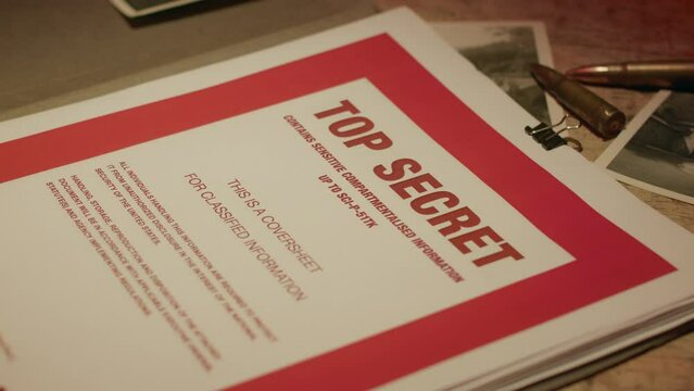 A retro manilla folder containing documents marked 'Top Secret' is seen on a wooden table lit by subdued light.