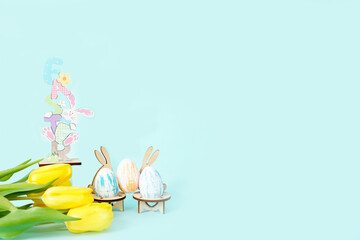 Statuette of a beautiful inscription Easter with colorful eggs and a bouquet of yellow tulips on a blue background. High quality photo