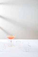 Glasses With orange Liquid and empty On white table with gray background, shadows, light rays, vertical 