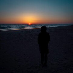 A young woman standing on a sea shore looking into a beautiful and colorful sunset on a calm as ice sea