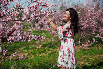woman in a dress by a flowering tree in the garden pink flowers rest on the street in the park