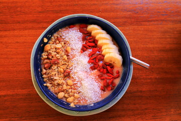 Plate with summer breakfast, fruit salad on brown table, recipe. Bowl food, vegetarian dish, top view. Fruit sweet mousse decorated with sliced bananas, almonds coconut flakes, nuts