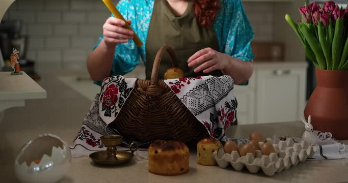 Woman preparing Easter basket with embroidered towel at kitchen home with tulips standing on the table. High quality photo