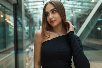 Beautiful fresh caucasian woman model in a fashion black one-shoulder top in a modern glass office building