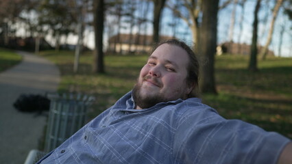 Portrait of a happy overweight man sitting at park bench looking at camera smiling during sunset