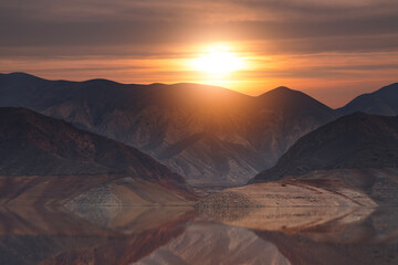 Beautiful sunset over the mountains and lake with reflection in the water. 