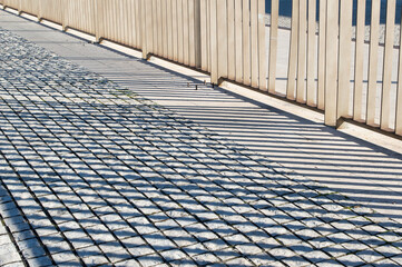 Shadow of a fence on the stone sidewalk, geometric pavement