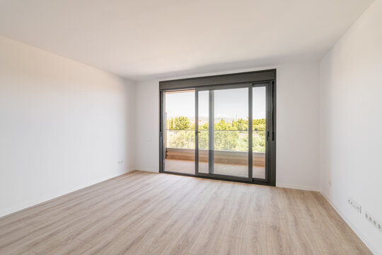 Spacious large room with wooden parquet structure and panoramic window overlooking beautiful landscape among complex of new buildings and balcony with elegant glass border. Mortgage and moving concept