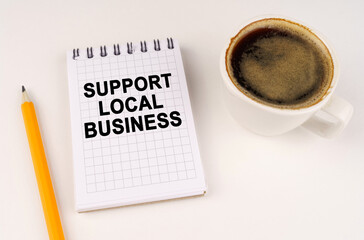 On a white surface, a cup of coffee, a pencil and a notepad with the inscription - Support local business
