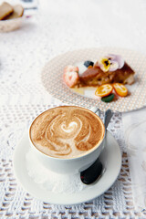 white porcelain cup of latte cappuccino coffee on the table in a cafe with a piece of cake in the background