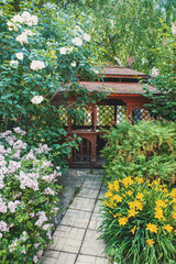 Fototapeta na wymiar gazebo in landscape design. Open wooden gazebo with lilac, yellow daylily and summer landscape on the background