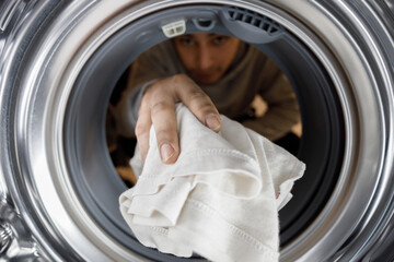Close-up of a young man putting clothes in the washing machine drum