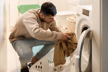 Young man putting clothes into washing machine 