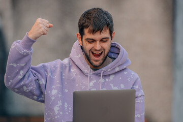 young man with laptop in the street with expression of success