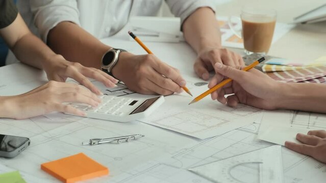 Cropped shot of hands of unrecognizable architects having discussion about floor plans and using calculator while working in team at office table
