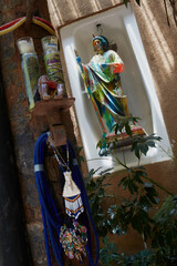 Muro de adobe con escultura religiosa  multicolor enmarcada en tina de baño  con textiles y veladoras.