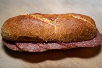 Crispy baguette bun with salami slices on a wooden board