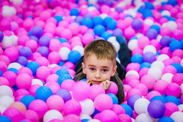 Fototapeta na wymiar A beautiful little smiling boy, a preschool child lies in a variety of multi-colored, colored plastic balls on the playground. Photography, portrait, childhood vacation concept.