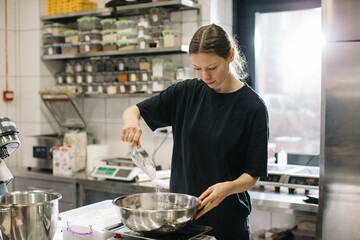 A woman cook works in a modern industrial kitchen. The process of making cakes in a bakery or cafe.