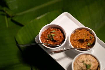 Three chutneys — ginger garlic chutney, tomato chutney, and peanut chutney — served fresh, against a backdrop of banana leaves.