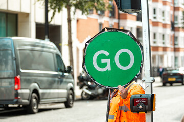 Road Construction Worker Holding a Green Go Sign to Indicate Safe Passage and Allow Traffic to Move...
