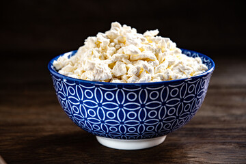 White fresh cottage cheese in a blue bowl on the kitchen table.